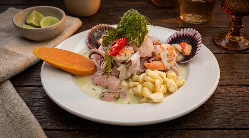 A vibrant ceviche dish with seafood, corn, sweet potato, and seaweed on a white plate.
