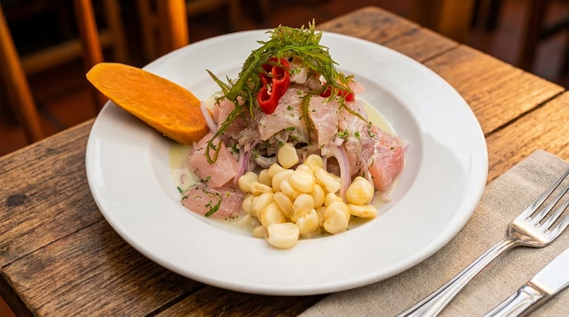 Peruvian ceviche with fish, red onion, corn, sweet potato, and chili on a white plate.